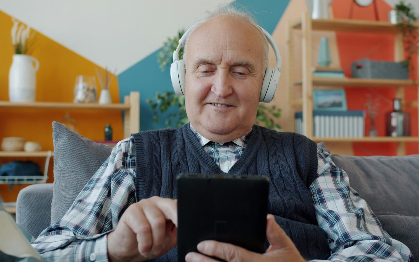 Starejši moški ima na glavi slušalke, posluša galsbo, v rokah ima pa pametni telefon