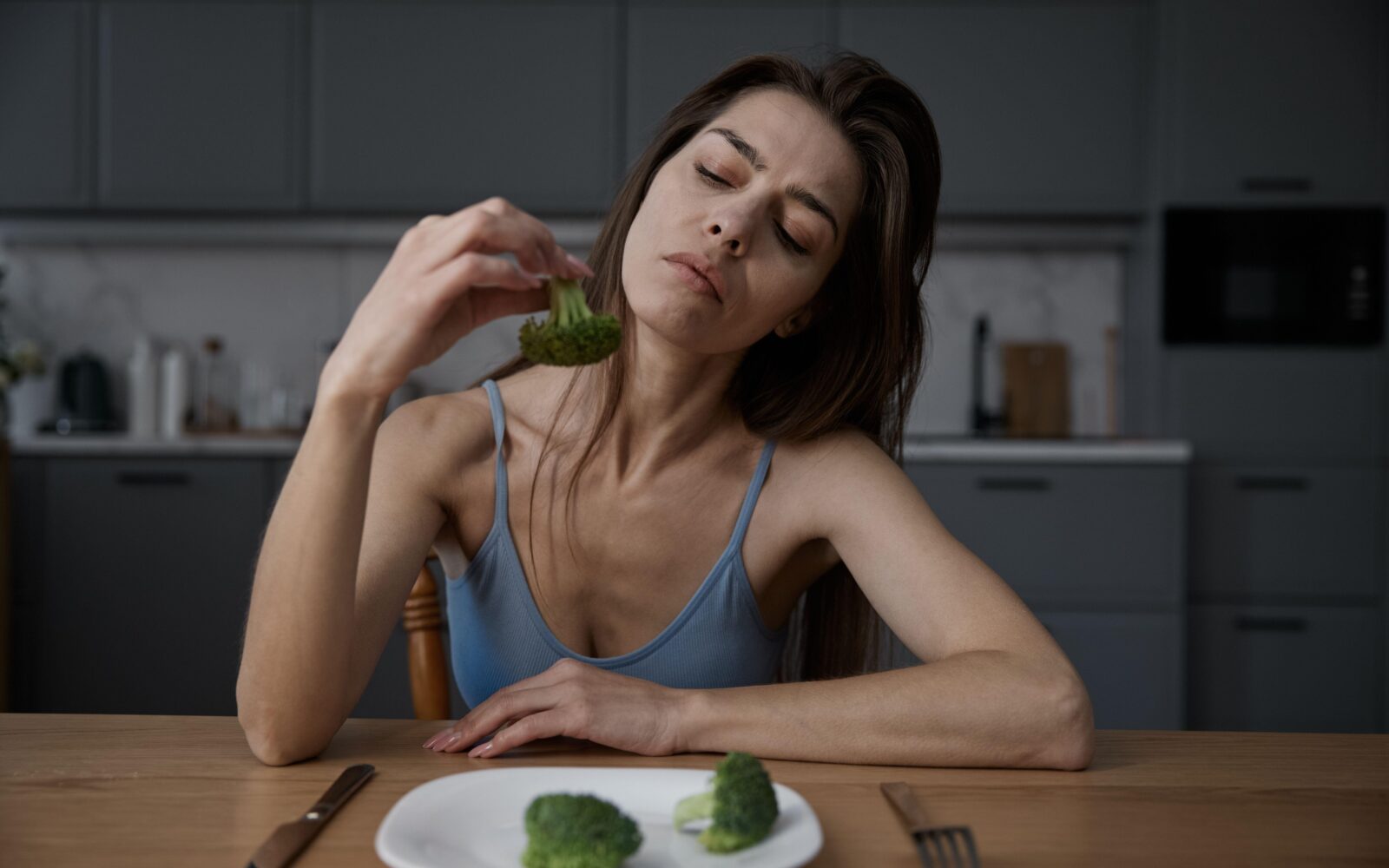 Zelo suha ženska z motnjo hranjenja ima na krožniku tri brokolije, enega gleda in razmišlja ali bi ga pojedla