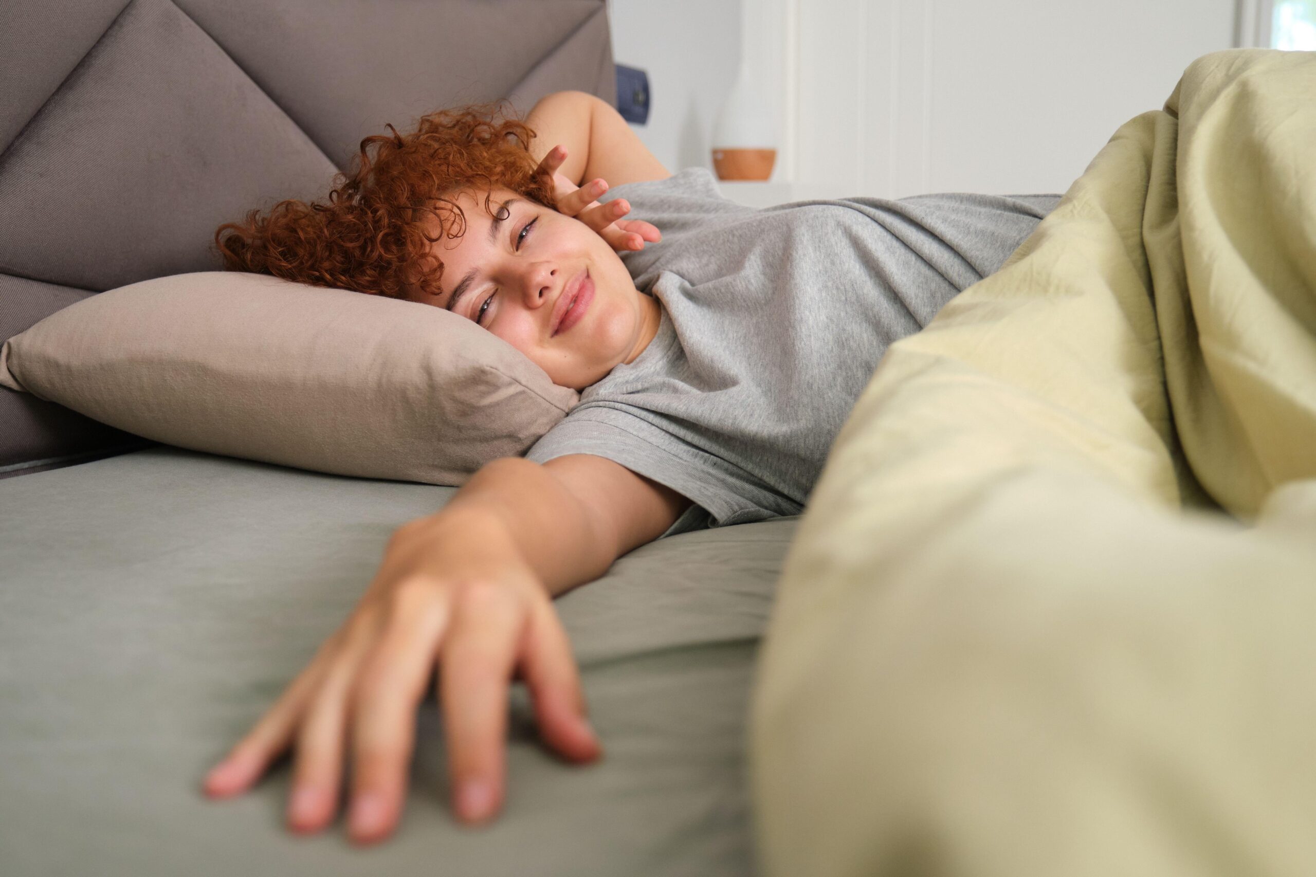 Mlada ženska dobre volje leži v postelji in se razteguje po kvalitetnem počitku.