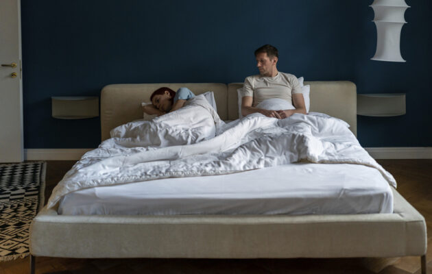 Moški in ženska v postelji. Ženska ima proti moškemu obrnjen hrbet, moški jo gleda. Simbolika težav v odnosu