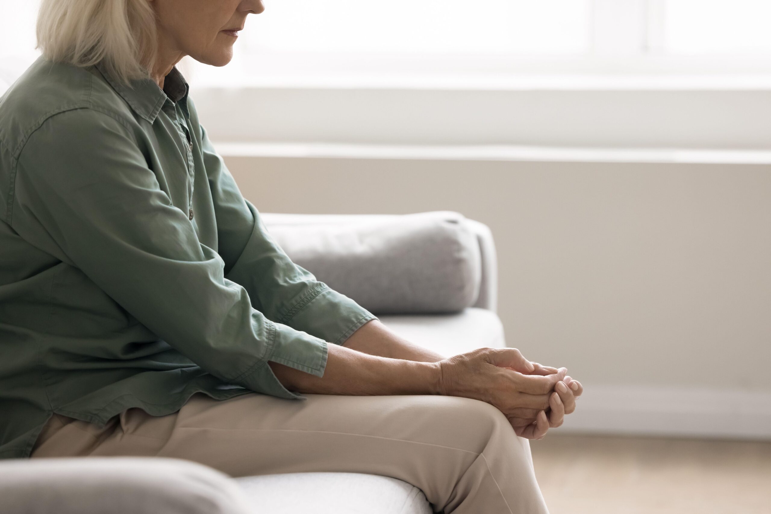 Ženska srednjih let sedi na kavču, utrujena zaradi stresa in čustvenih sprememb, povezanih s hormonskimi spremembami.