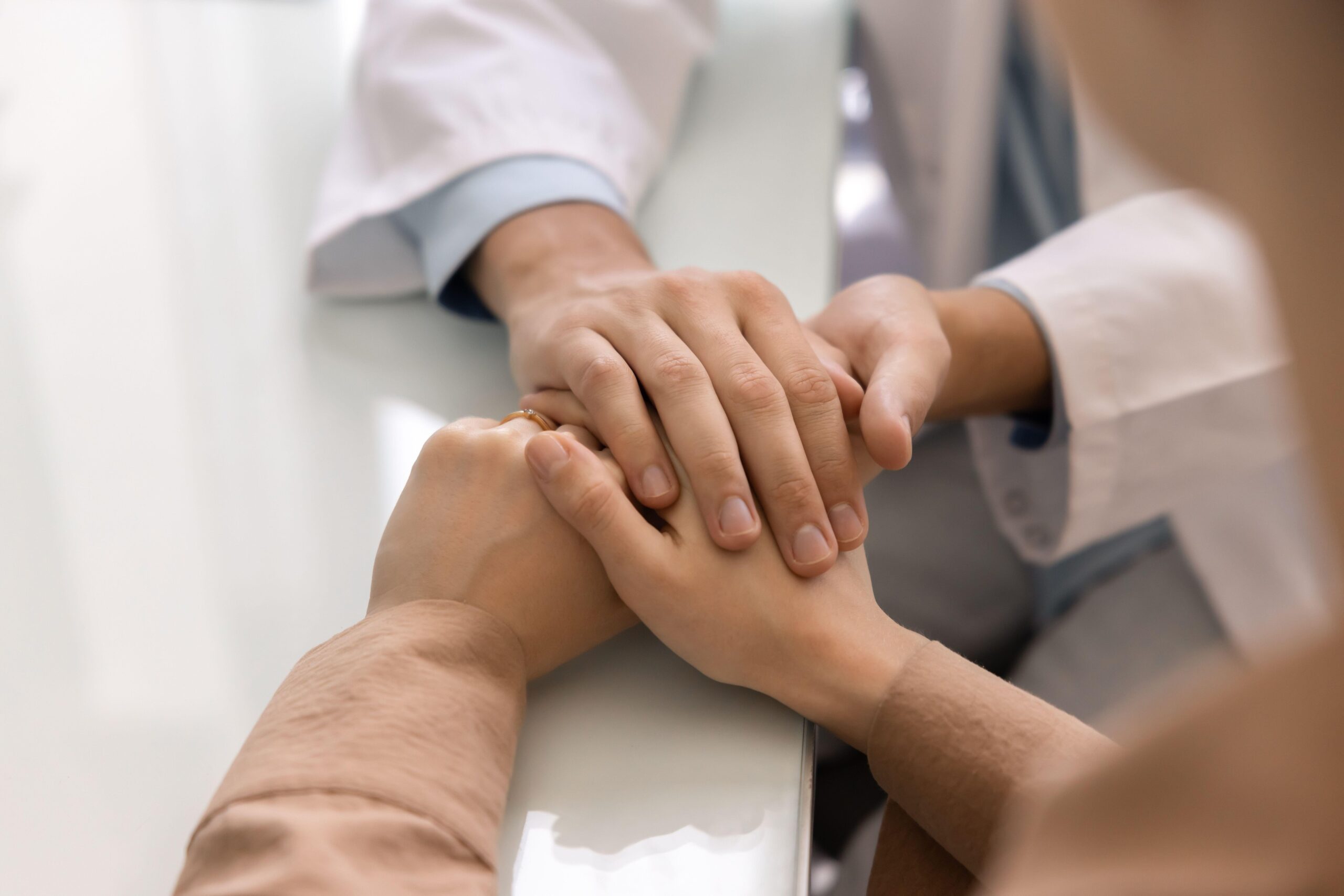 Ginekolog drži za roko pacientku, prikaz zaupanja, strokovne podpore in svetovanja.