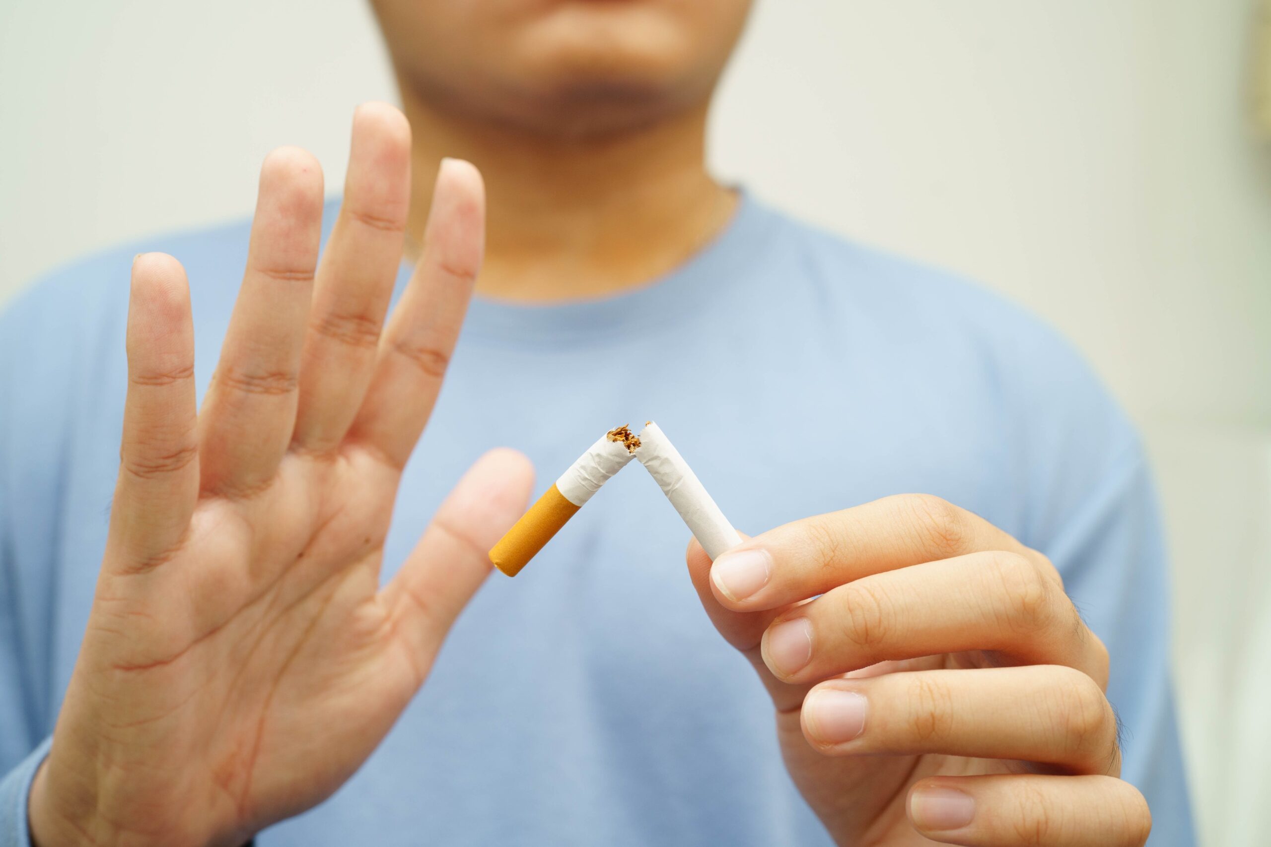 Moški v rokah drži zlomljen cigaret in kaže z roko: stop kajenju