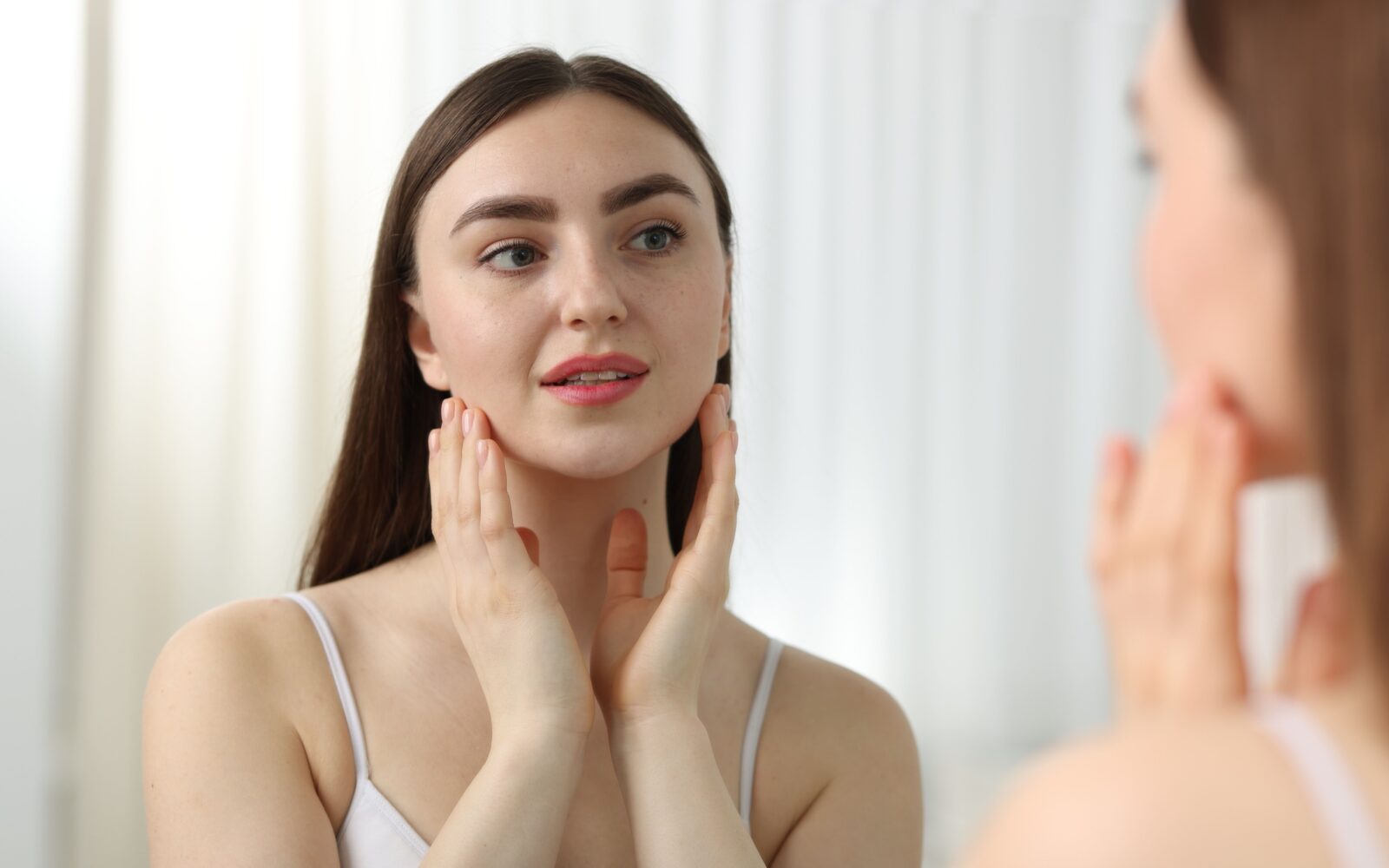 Ženska s sijočo kožo se gleda v ogledalo - posledica izogibanja alkoholu