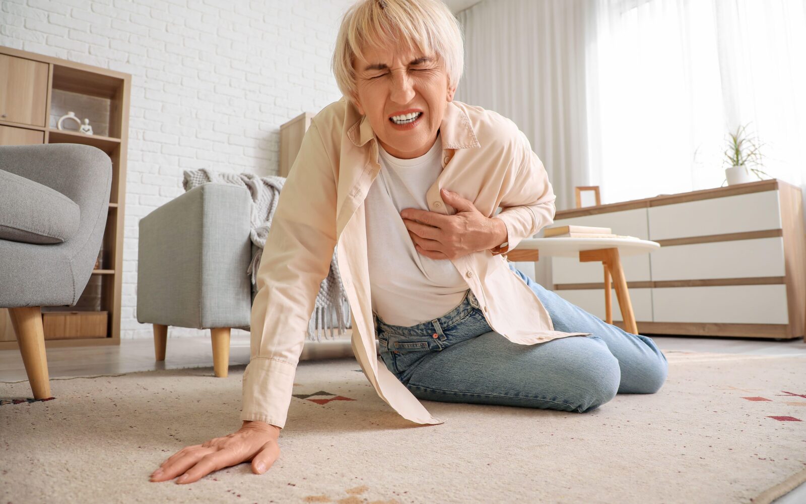 Starejša ženska se drži za srce, je padla po tleh, simbolični prikaz srčnega zastoja, srčnega infarkta, srčne kapi