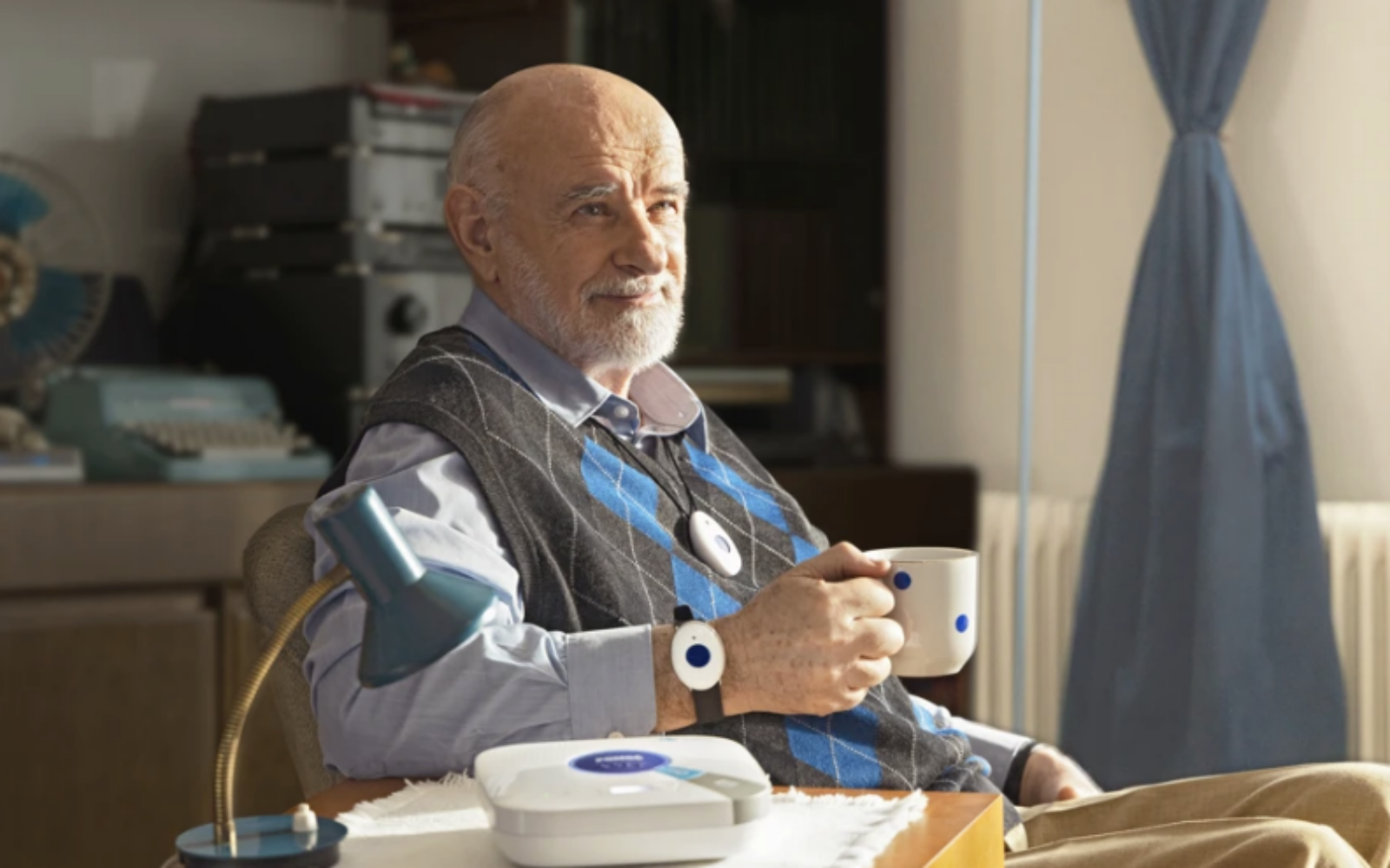 Starejši gospod sedi v fotelju v na svojem domu, a je varen s storitvijo e-oskrba.