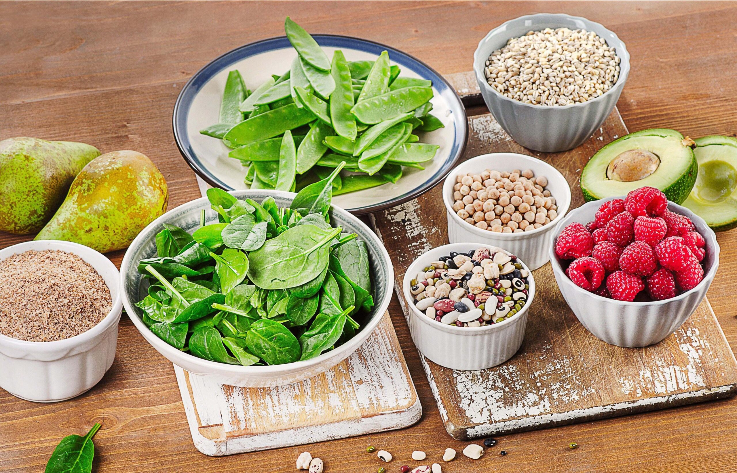 Živila, bogata z ogljikovimi hidrati in vlakninami, na leseni deski - maline, avokado, oreščki, listnata zelenjava, hruške, semena