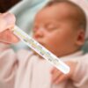 V ospredju termometer, ki kaže povišano temperaturo, v ozadju dojenček. Simbolika bolnega dojenčka