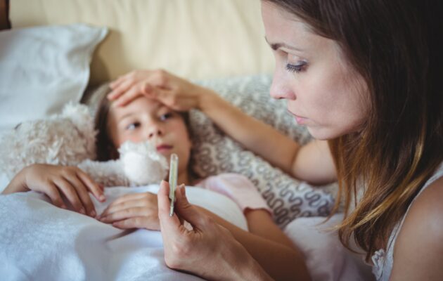 Bolna deklica leži, mati ji je izmerila temperaturo, v rokah drži termometer in jo drži za čelo