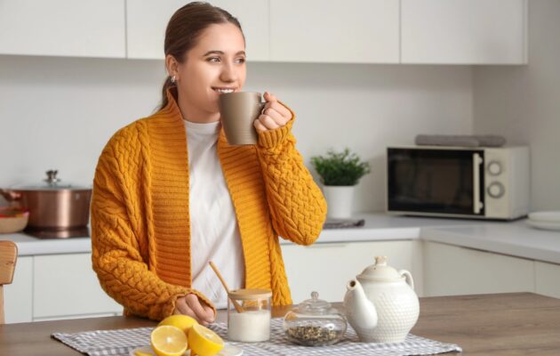 Ženska v kuhinji pije čaj z limono.