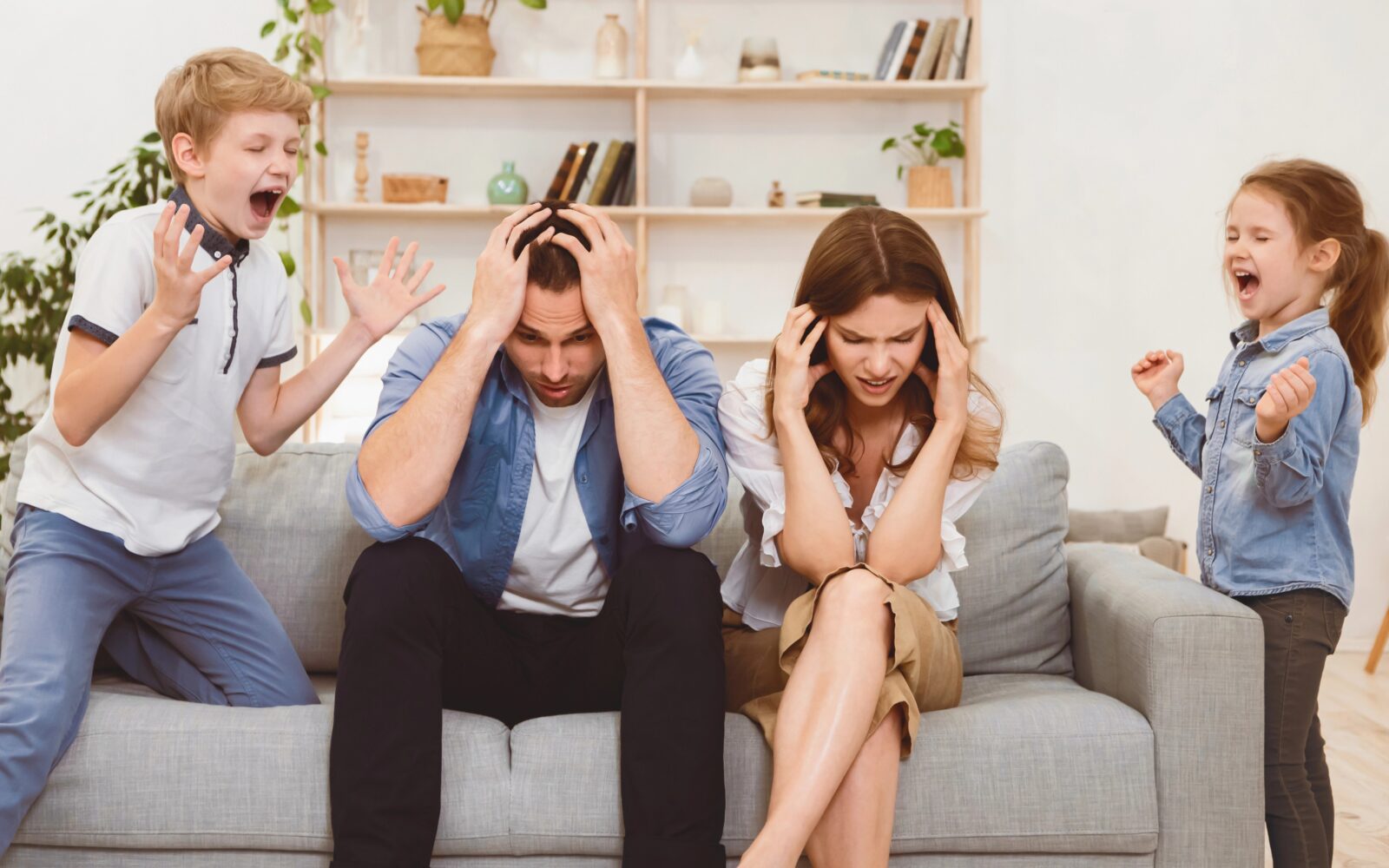 Izčrpana starša medtem ko otroka kričita, vsakodnevni družinski kaos doma