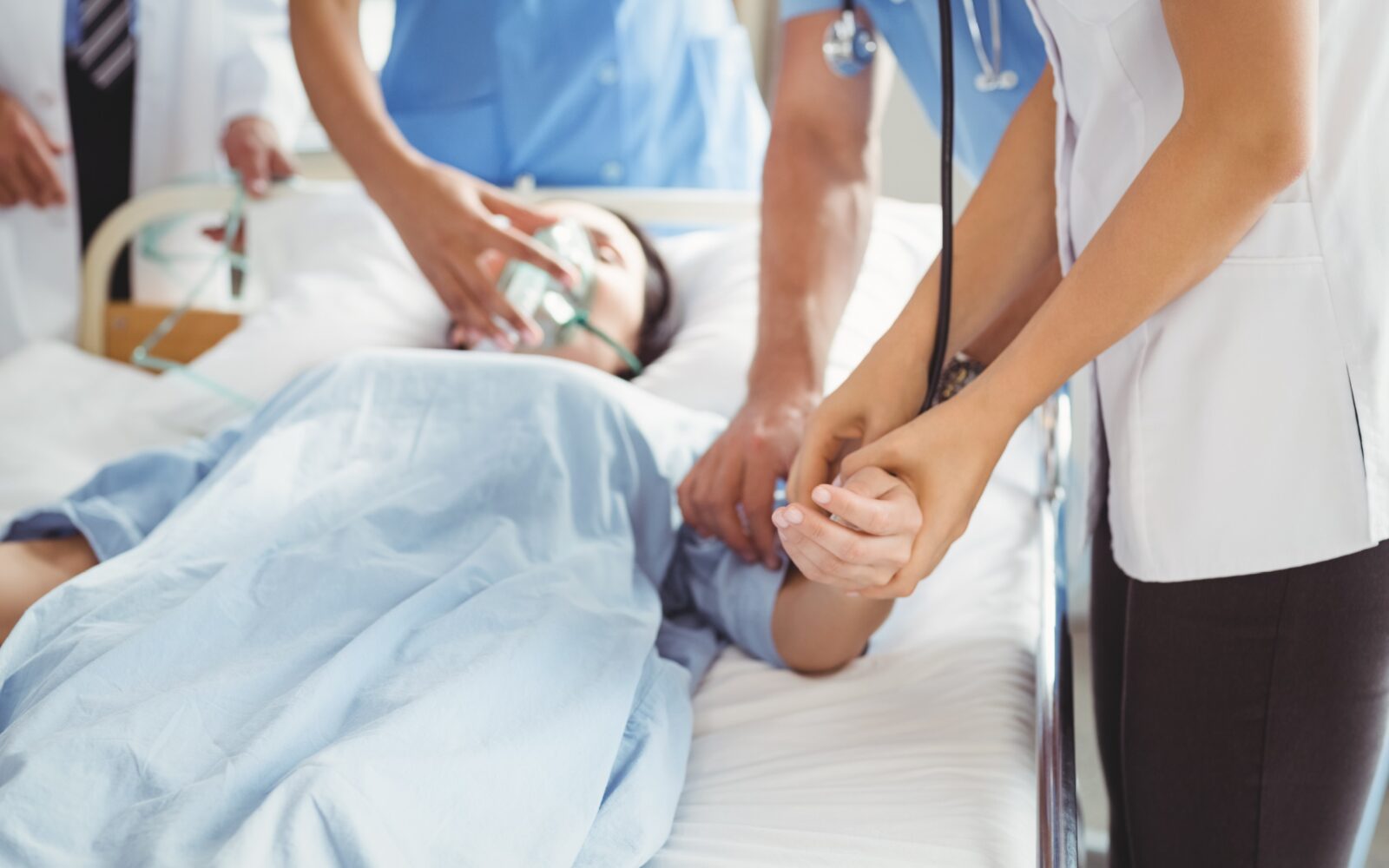 Oseba v nezavesti leži v bolniški postelji, okoli nje so zdravnik in zdravstveni tehniki