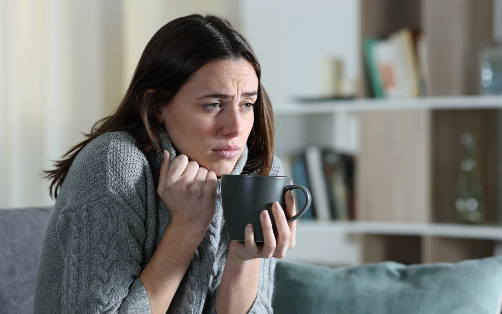 Žensko zebe, slabo se počuti, v rokah drži skodelico toplega napitka