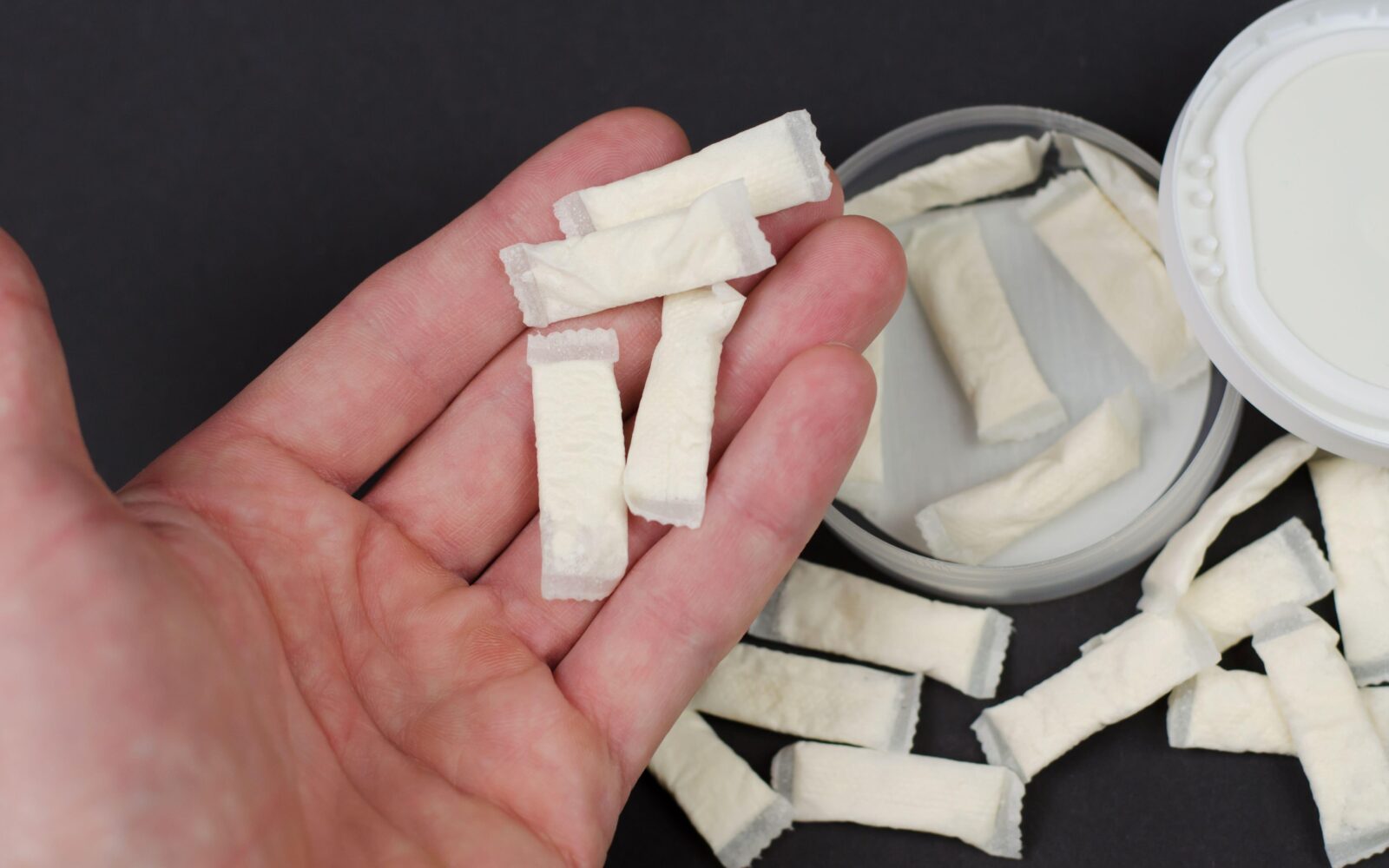 Na mizi je škatlica z nikotinskimi vrečkami, zraven pa roka, z nekaj temi vrečkami