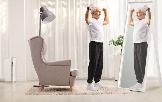 Starejši moški se gleda v ogledalu, roke ima dvignjene, simbol moči