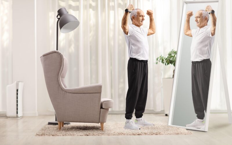 Starejši moški se gleda v ogledalu, roke ima dvignjene, simbol moči