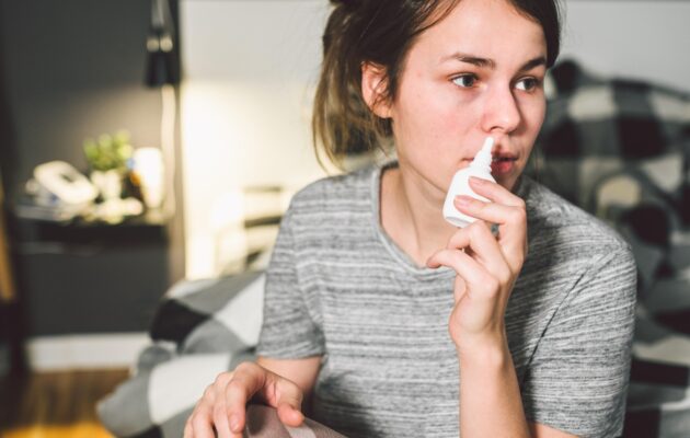 Ženska si ponoči lajša zamašen nos z nosnim pršilom v spalnici