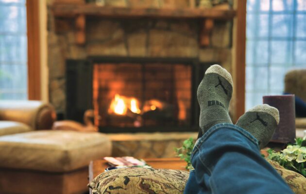 Nekdo sedi doma pred kaminom, v modrih jeans hlačah in sivih nogavicah