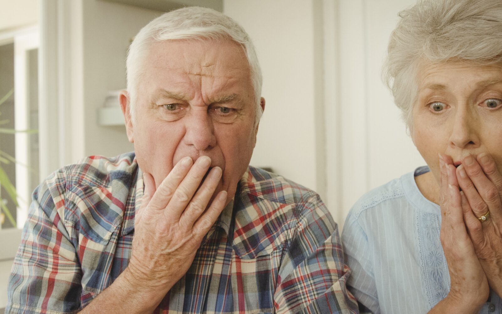 Starejši moški ni ženska presenečeno gledata v nekaj, moški ima od začudenosti roko pred usti