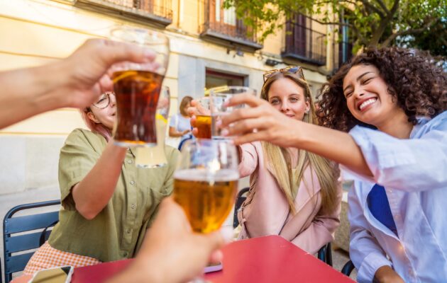 Skupina prijateljev sedi za mizo zunaj in nazdravlja - eni s pivom, drugi z vodo, ostali z gaziranimi pijačami - kaj je najboljša izbira?