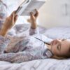 Mlada ženska leži na postelji, oblečena v pižamo in bere knjigo - preprosta aktivnost s številnimi pozitivnimi učinki za telo in možgane