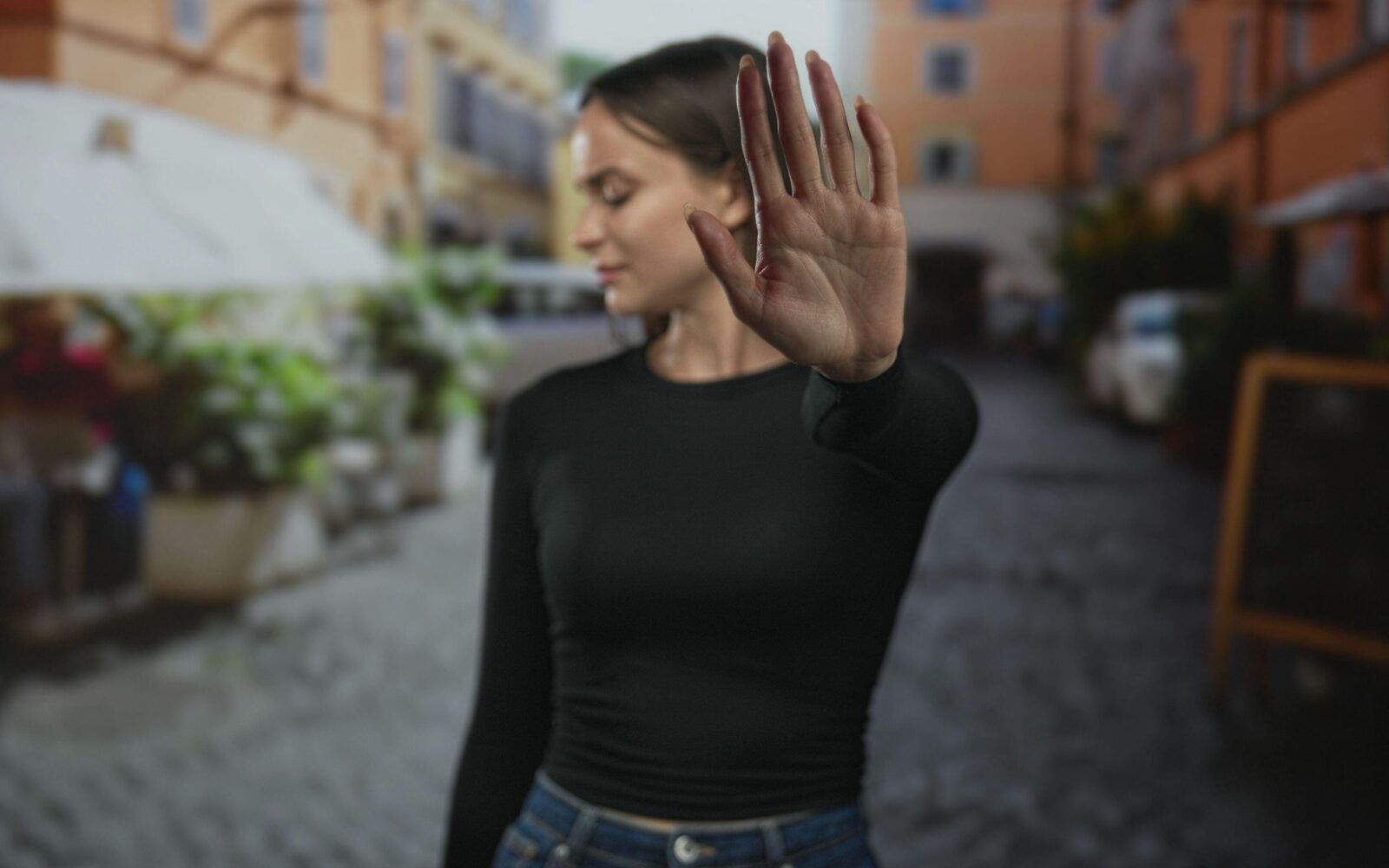 Ženska v urbanem okolju z dvignjeno dlanjo jasno postavlja mejo, simbol opolnomočenja skozi samoobrambo ESD in osebne varnosti žensk.