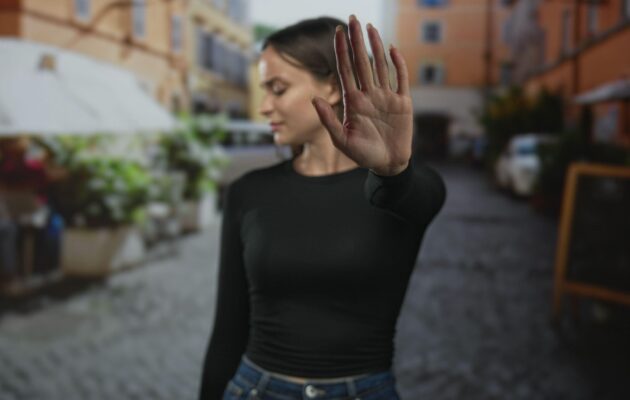 Ženska v urbanem okolju z dvignjeno dlanjo jasno postavlja mejo, simbol opolnomočenja skozi samoobrambo ESD in osebne varnosti žensk.