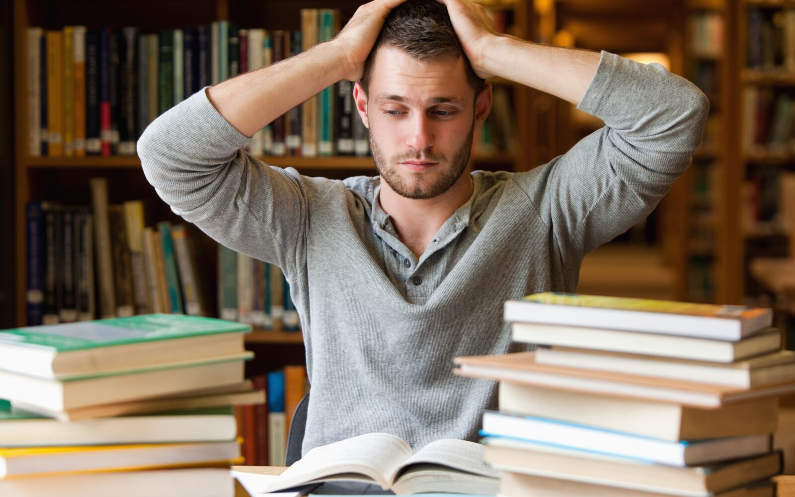 Mlad moški se drži za glavo, pred sabo ima številne knjige, preveč dela