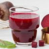 Kozarec soka rdeče pese na mizi ob sveži rdeči pesi, naravni vir nitratov za zniževanje krvnega tlaka.
