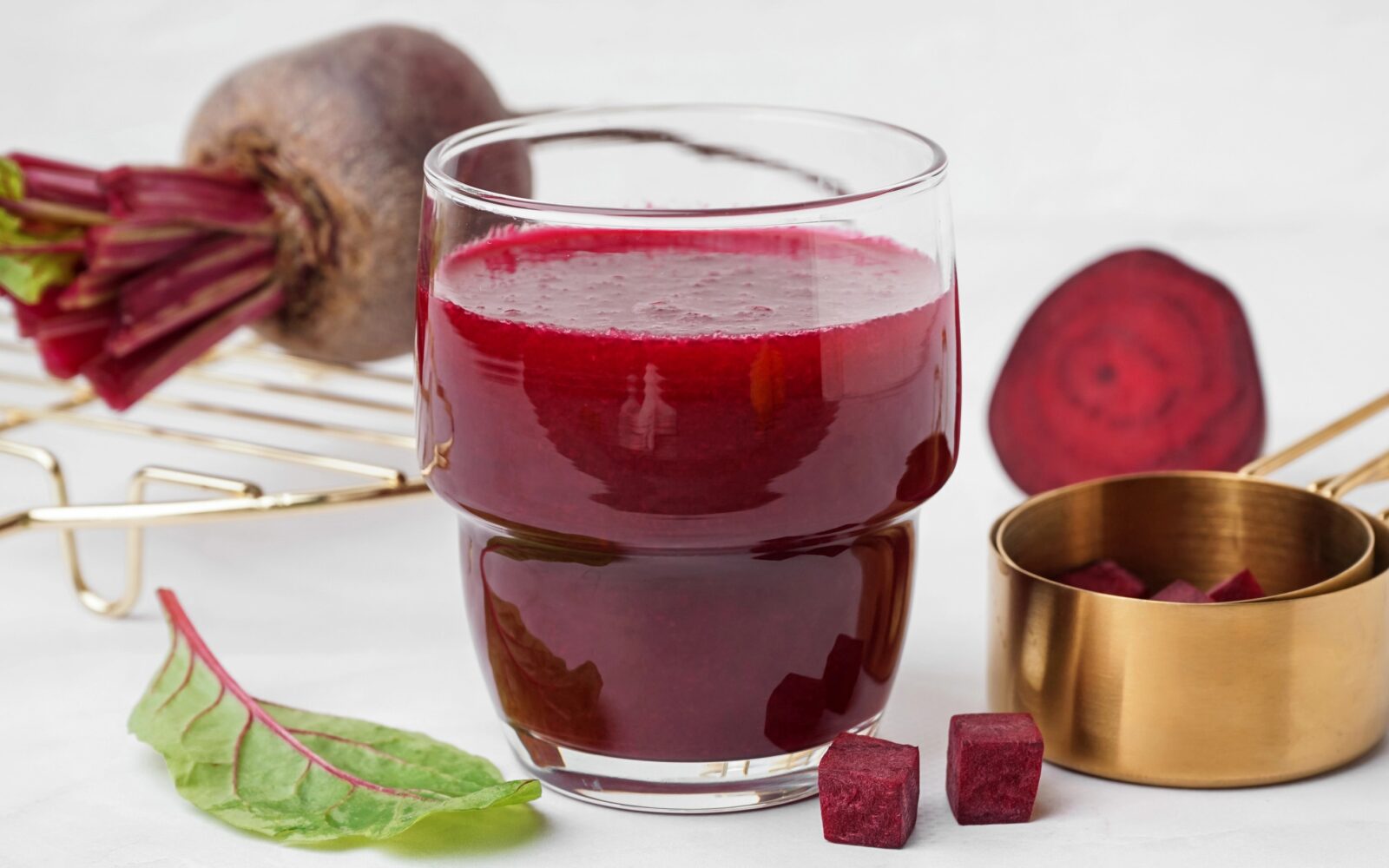 Kozarec soka rdeče pese na mizi ob sveži rdeči pesi, naravni vir nitratov za zniževanje krvnega tlaka.