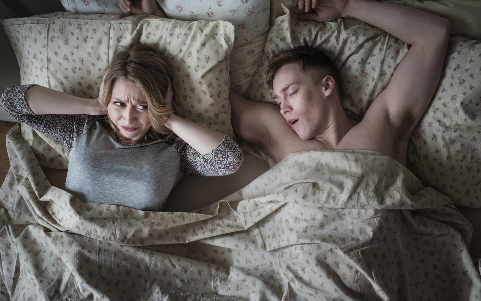 Moški in ženska ponoči v postelji, ženska ne more spati (in si zatiska ušesa) zaradi tega, ker moški smrči.