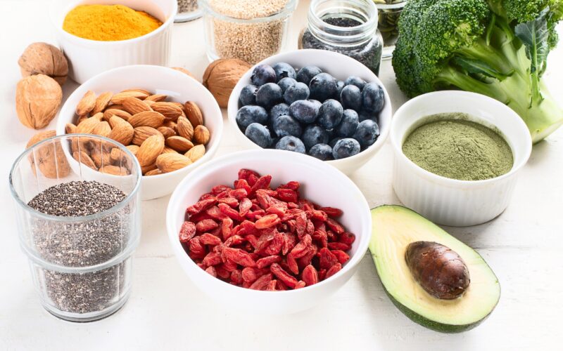 Različna superživila zložena na mizi - na sliki vidimo goji jagode, chia semena, avokado, matcho, brokoli, mandlje, kurkumo, borovnice, orehe