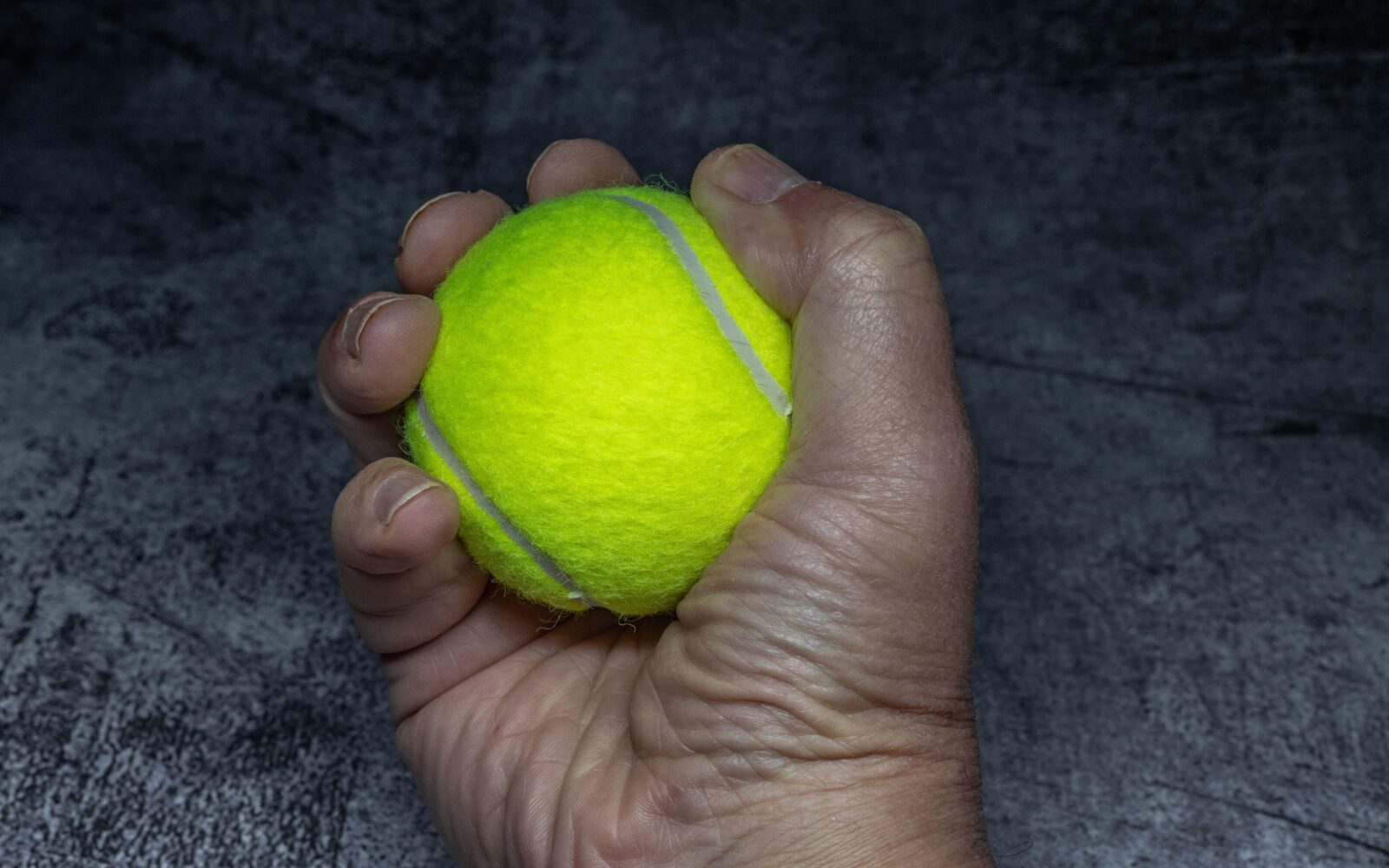 Moška roka, ki stiska teniško žogico - test moči oprijema, ki je pokazatelj zdravega staranja.