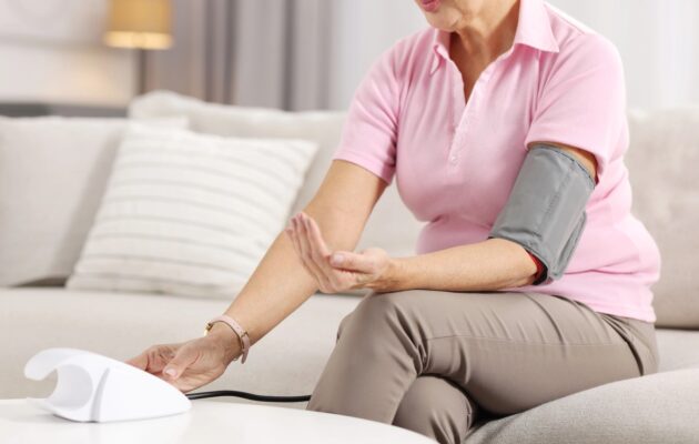 Starejša ženska si meri krvni tlak v domači sobi
