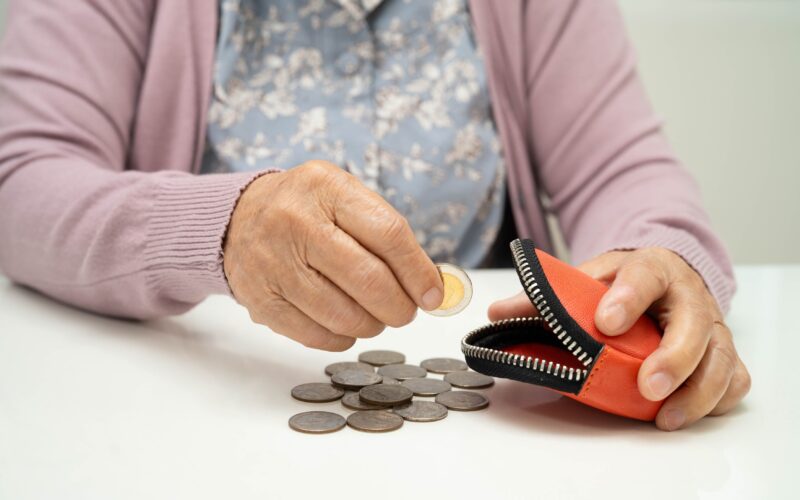 Starejša oseba z denarnico v roki, ki ponazarja demenco, izgubo presoje in tveganja pri ravnanju z denarjem