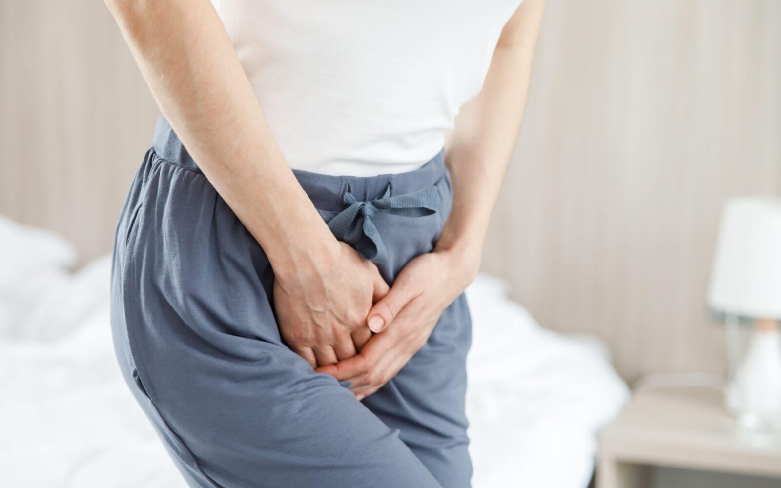 Ženska z rokami na spodnjem delu trebuha kaže nelagodje zaradi vraščene dlake na intimnem predelu